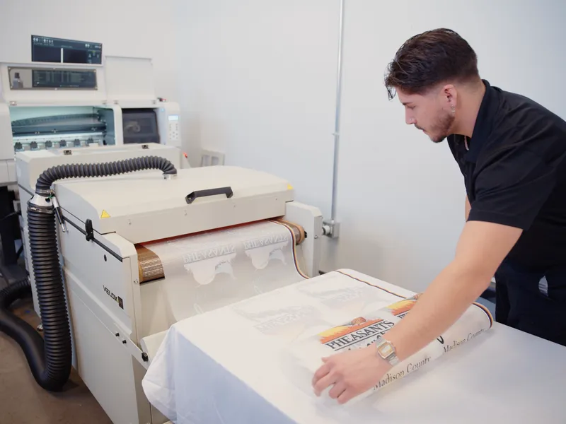 Operator at heat press applying Pheasants Forever DTF transfer